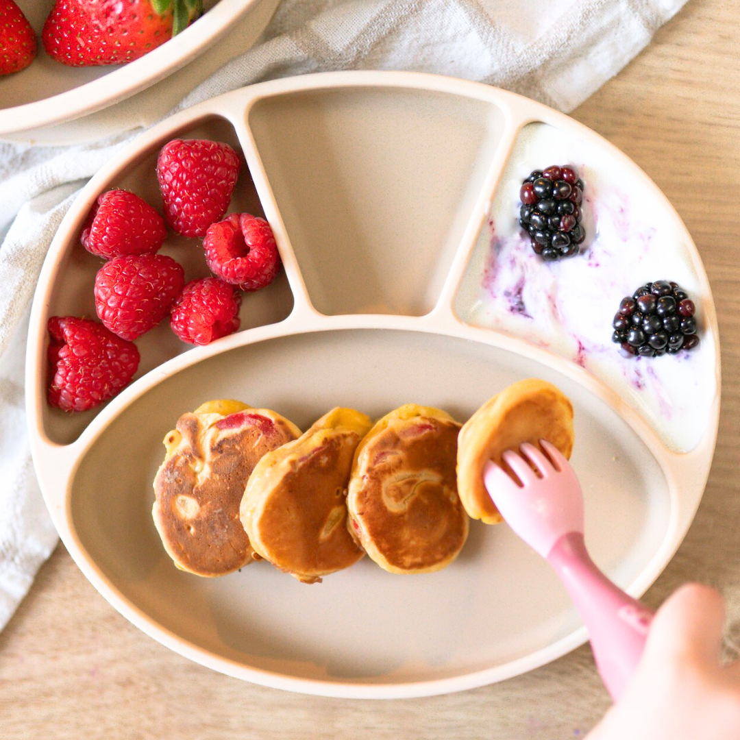 Baby-led weaning plate with Scotch pancakes, raspberries, and blackberries in yoghurt.