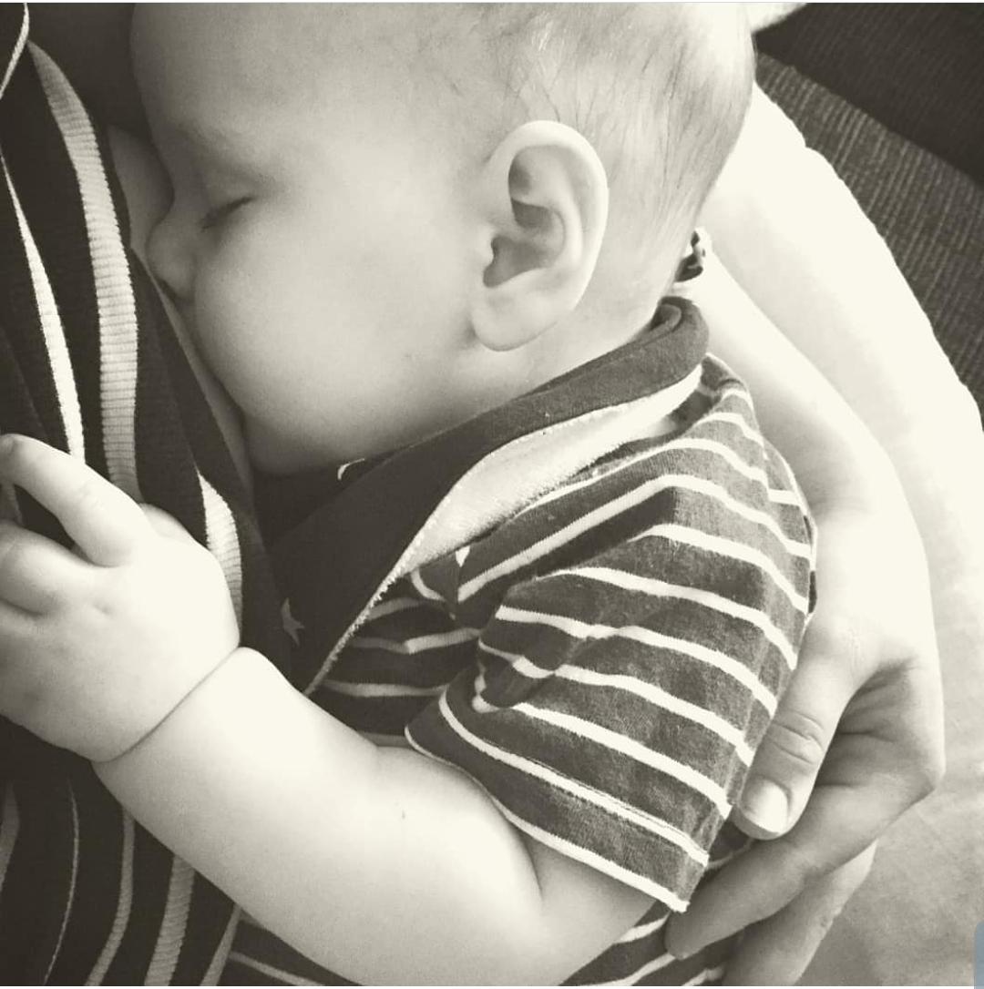 Close-up of a baby sleeping peacefully on a parent's chest, wearing a striped top.