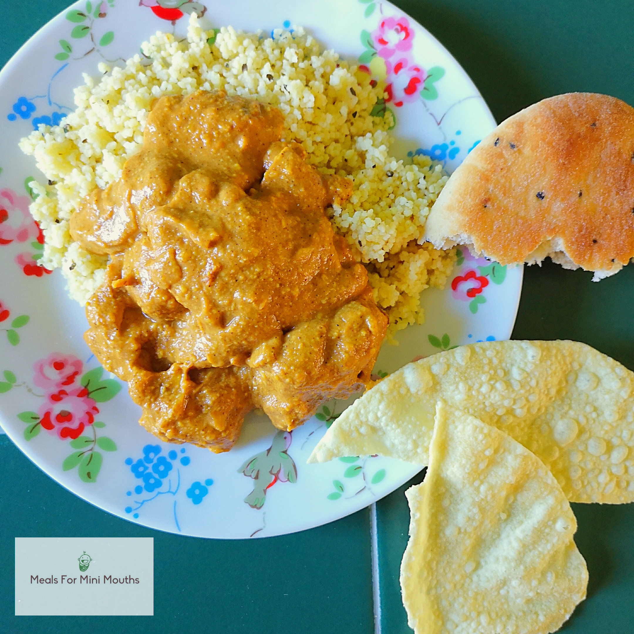 Mild chicken curry with couscous, naan bread, and poppadoms on a floral plate.