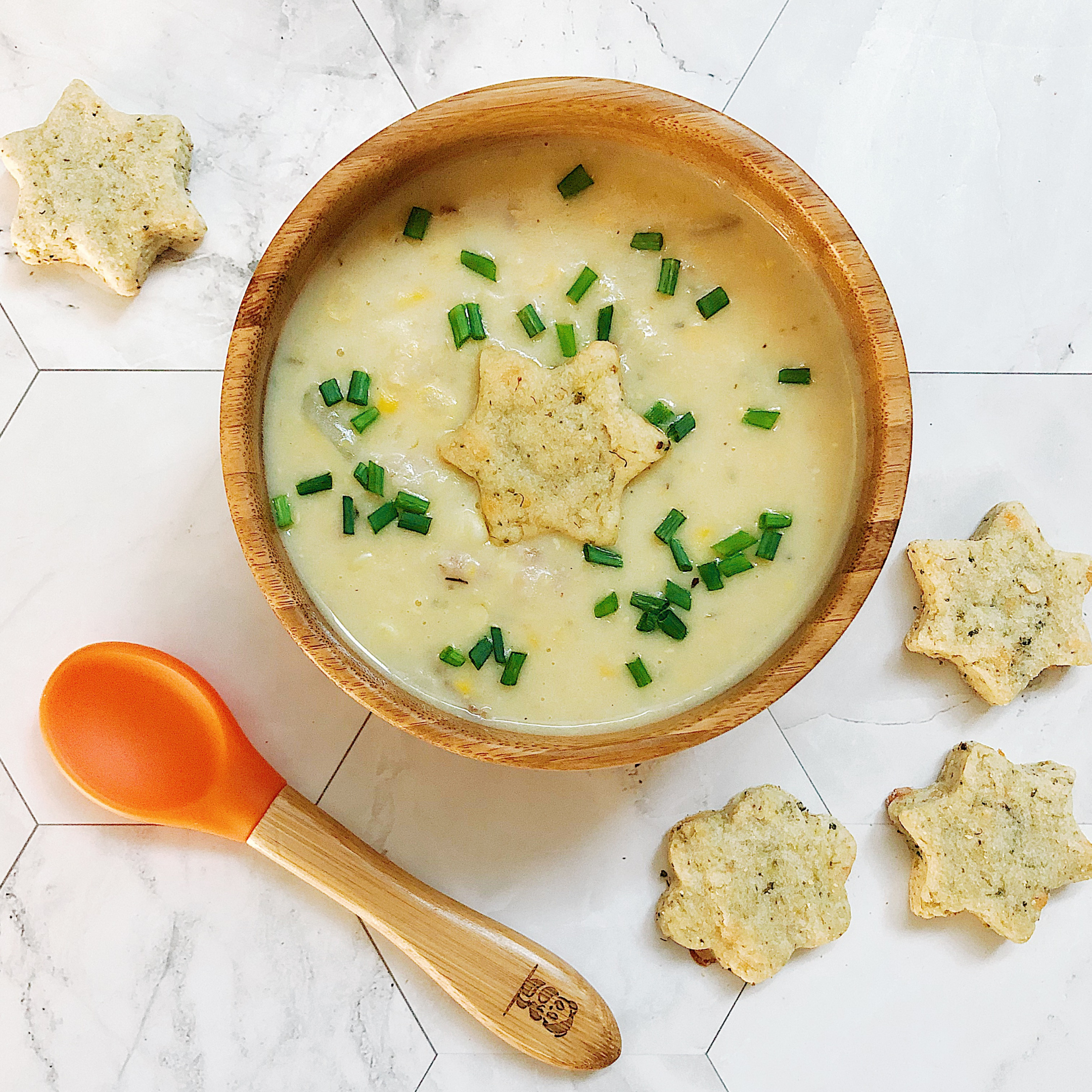 Creamy corn chowder in a wooden bowl, garnished with chives and star-shaped crackers.