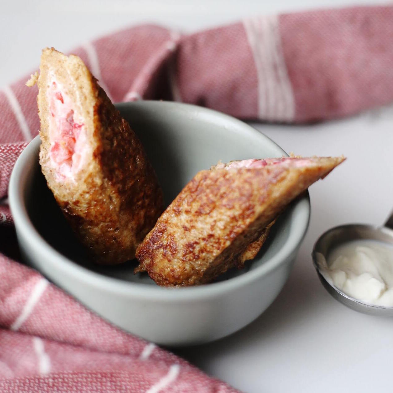 Two golden-brown fruity French toast rolls in a grey bowl, with a pink striped tea towel.