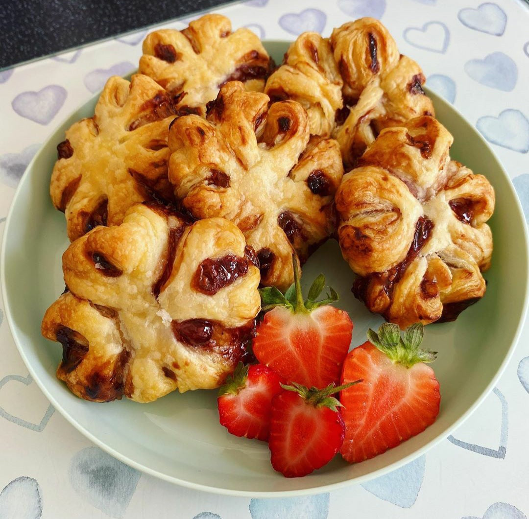 Golden brown jammy puff pastries with strawberry filling, served with fresh halved strawberries.