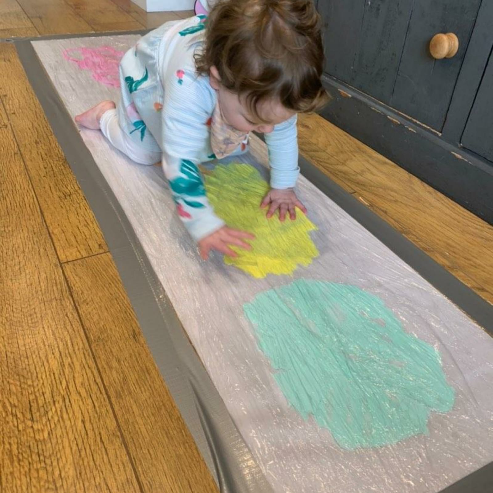 Toddler in pyjamas creating mess-free art with colourful paint under clear film.
