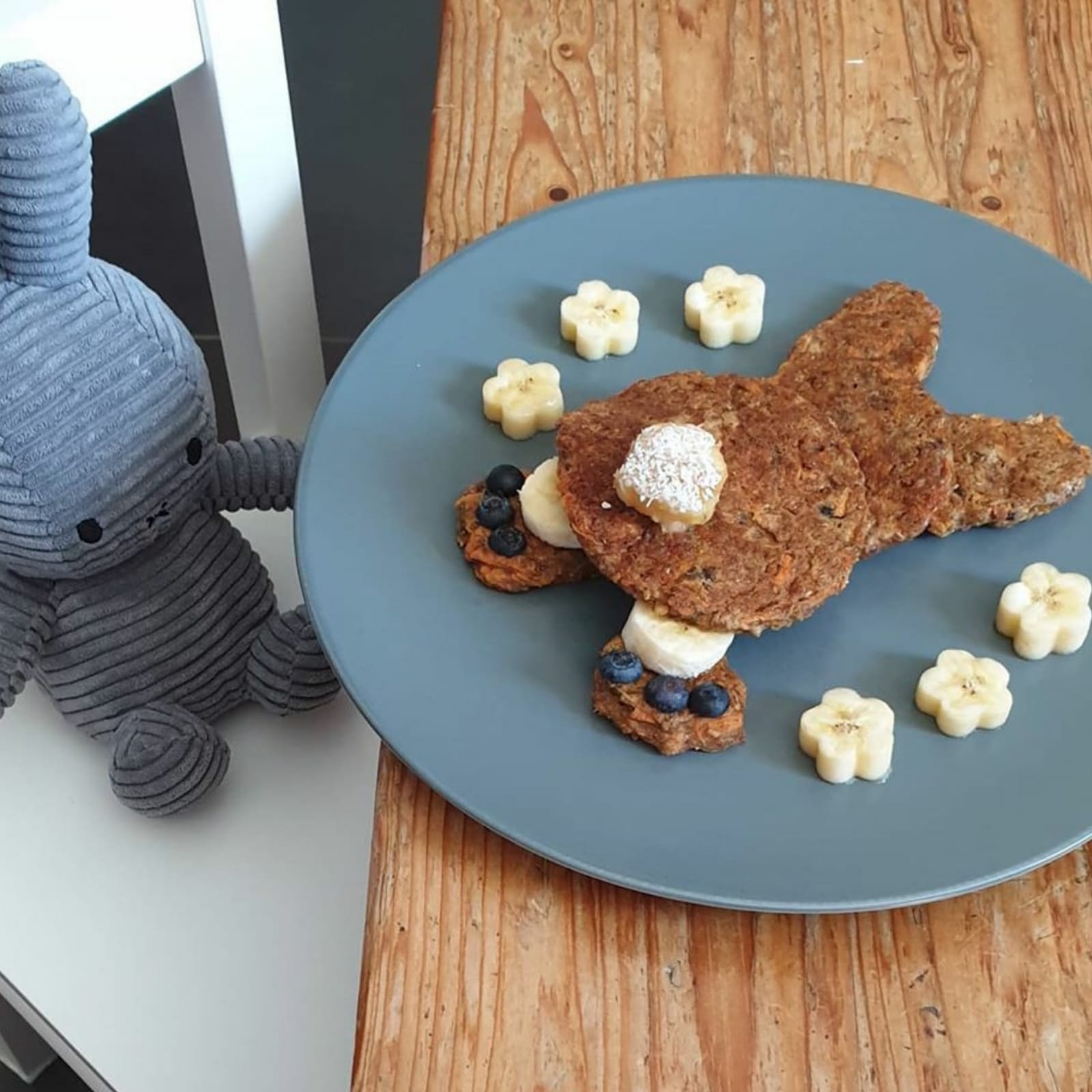 Fluffy carrot pancakes shaped like a bunny, garnished with banana slices and blueberries.