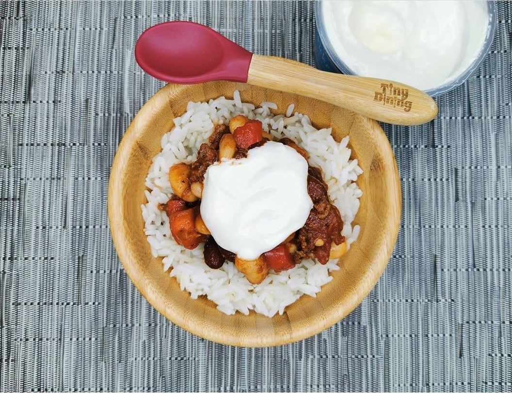 Mild chilli con carne with rice and a dollop of natural yoghurt in a wooden bowl.