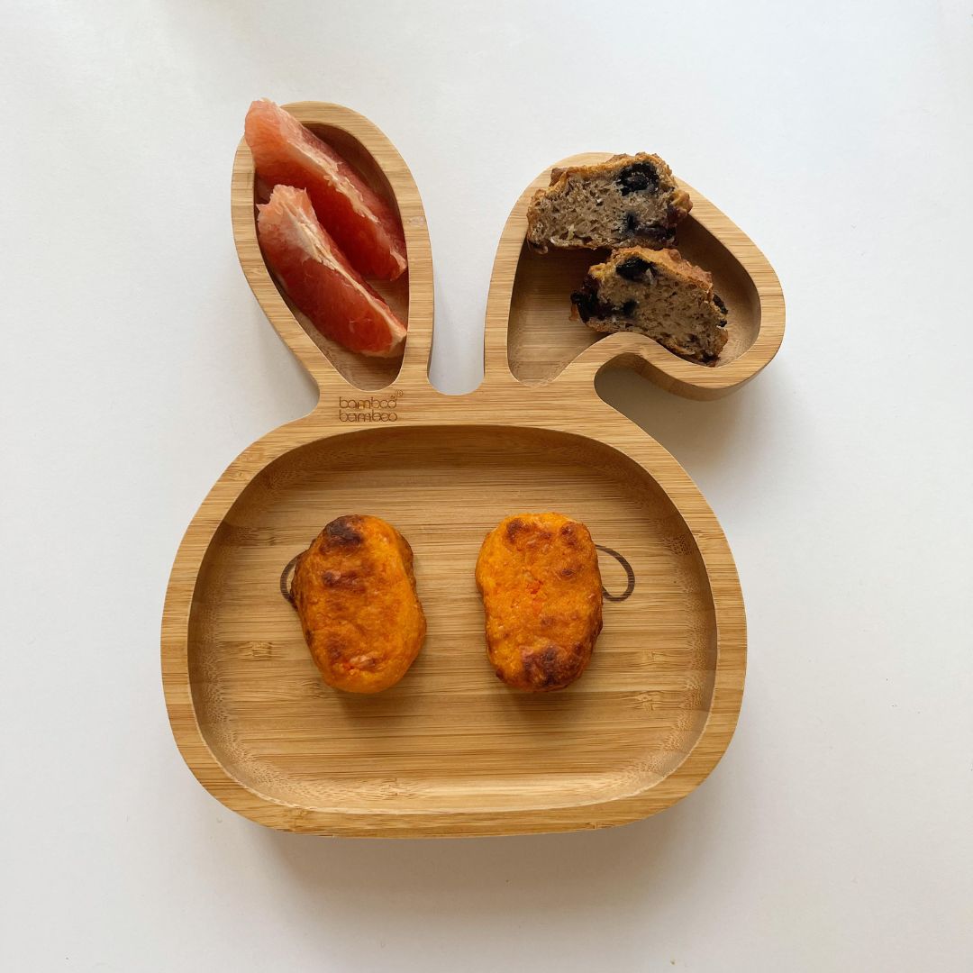 Two golden-brown cheesy sweet potato and carrot tots on a bamboo bunny plate with grapefruit and cake.