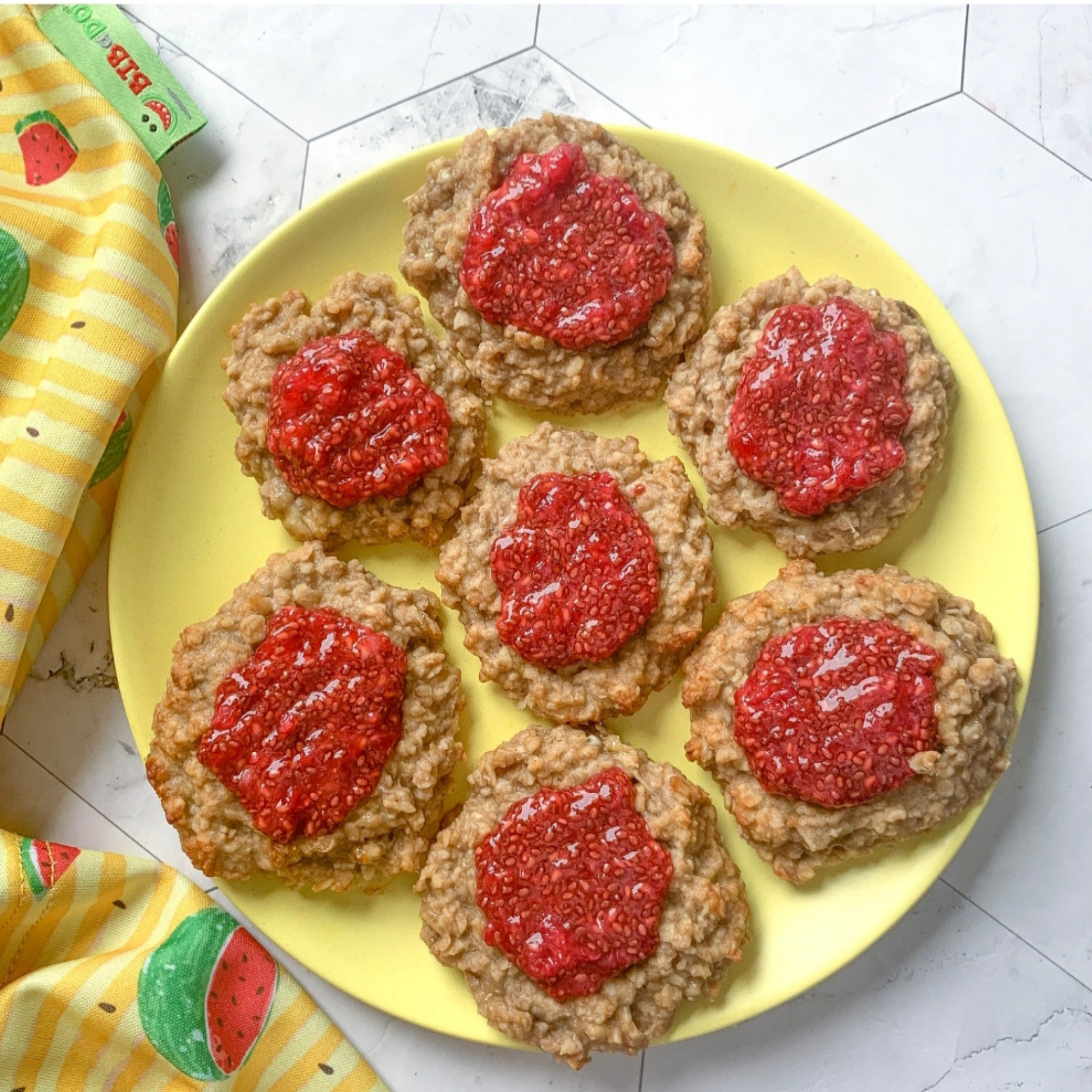 Homemade Jammy Dodger-style oat biscuits with vibrant raspberry jam on a yellow plate.