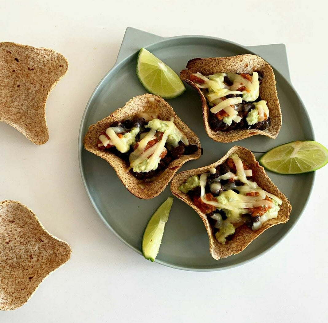 Three butternut squash and black bean tacos in wholemeal tortilla cups with melted cheese and lime wedges.