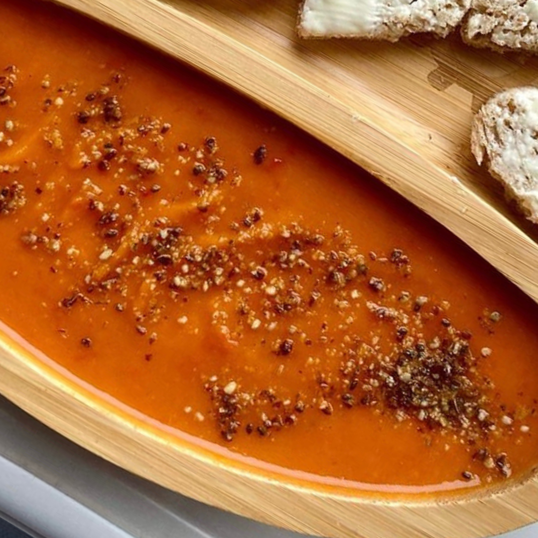 Vibrant butternut squash and red pepper soup in a wooden bowl, topped with black pepper, served with buttered bread.