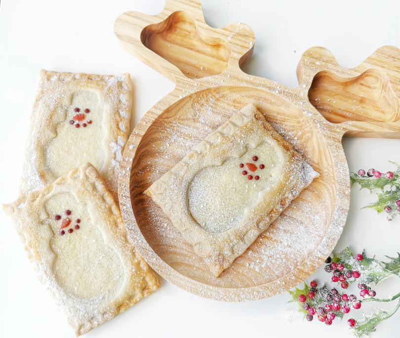 Flaky pastry snowman cheesecake slices dusted with icing sugar on a wooden reindeer plate.