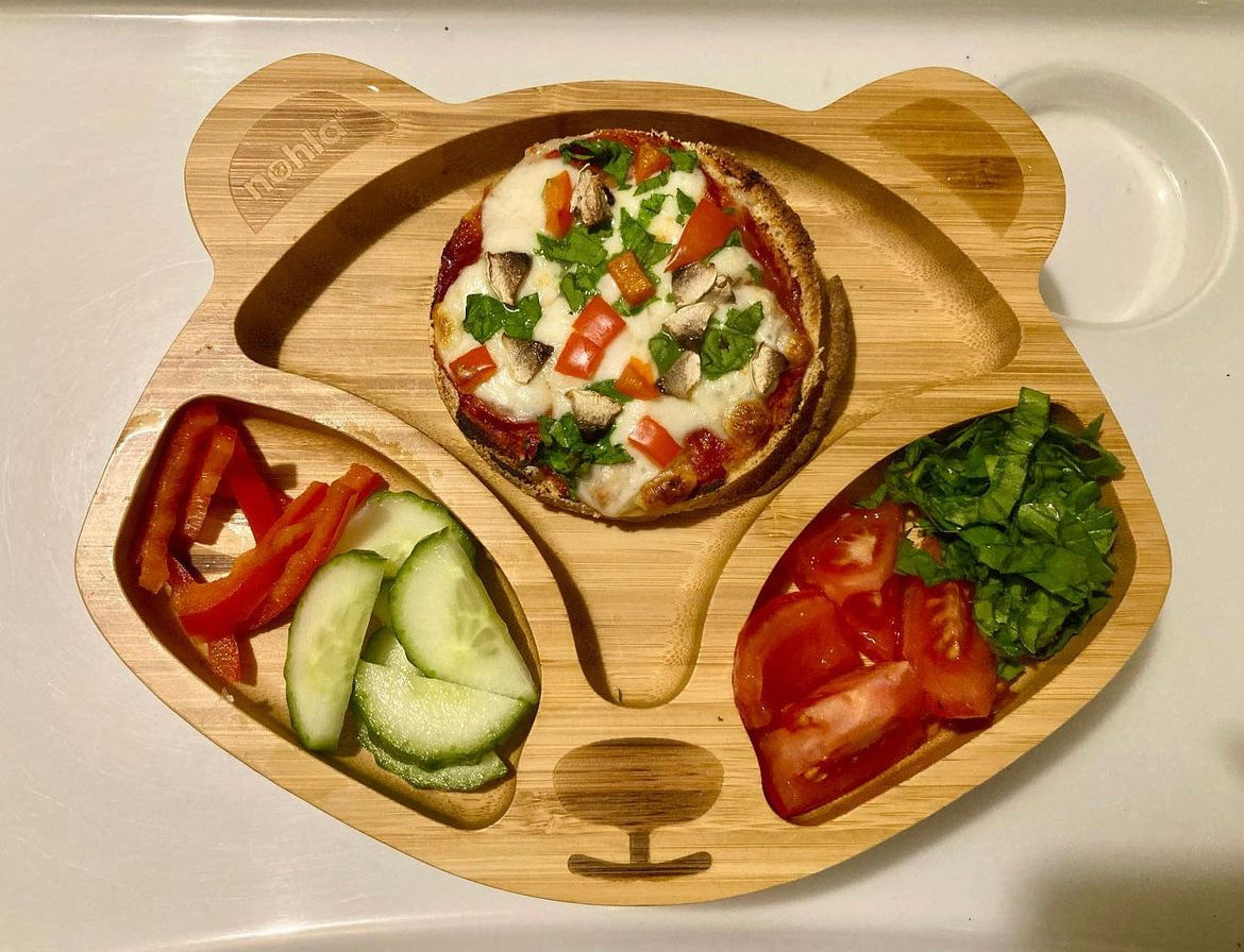 Muffin pizza with melted cheese, mushrooms, and red peppers on a bear-shaped bamboo plate.