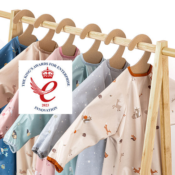 The King's Awards for Enterprise 2023 Innovation logo over a rack of colourful long-sleeved baby bibs.