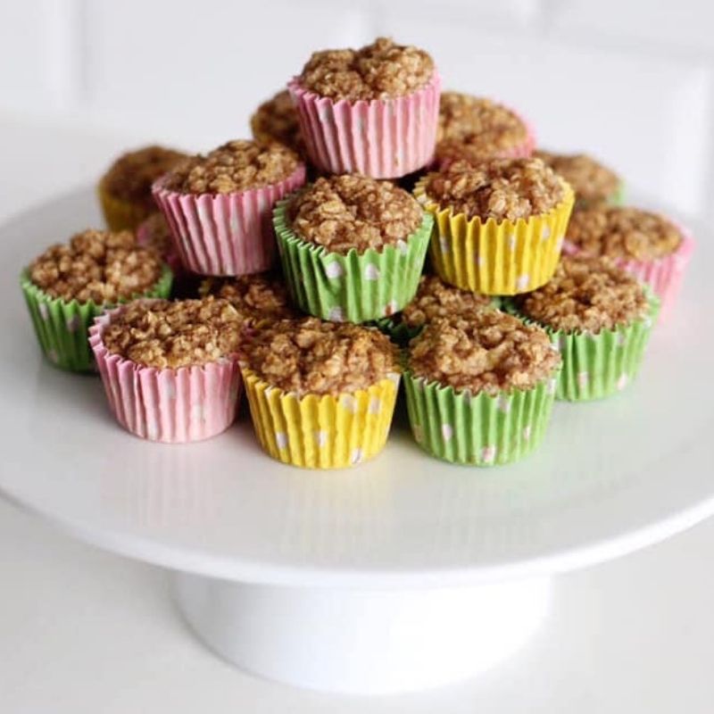 Pile of mini porridge bakes in colourful pink, green, and yellow cupcake cases on a white cake stand.