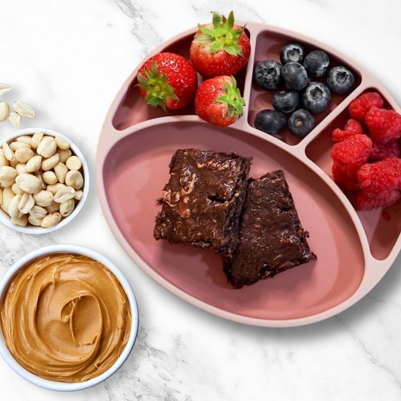 Pink silicone plate with peanut butter swirl brownies, strawberries, blueberries, and raspberries.
