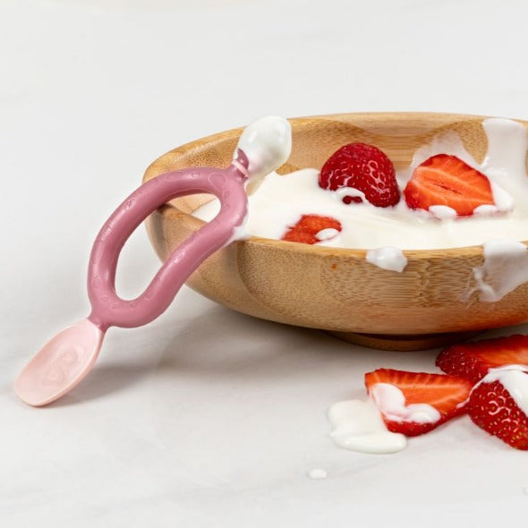 Pink silicone Dippit™ baby spoon and textured dipper in a wooden bowl with yogurt and strawberries. - Product image
