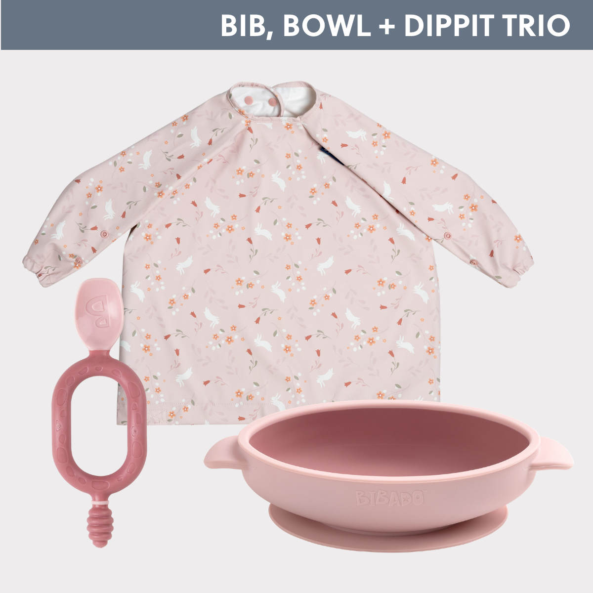 Pink long-sleeved weaning bib with bunny and floral print, matching silicone suction bowl, and soft Dippit spoon. - Product image