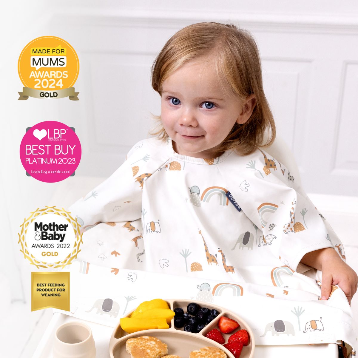 Toddler in a white short-sleeve coverall bib with a giraffe and rainbow print, eating from a divided plate. - Product image