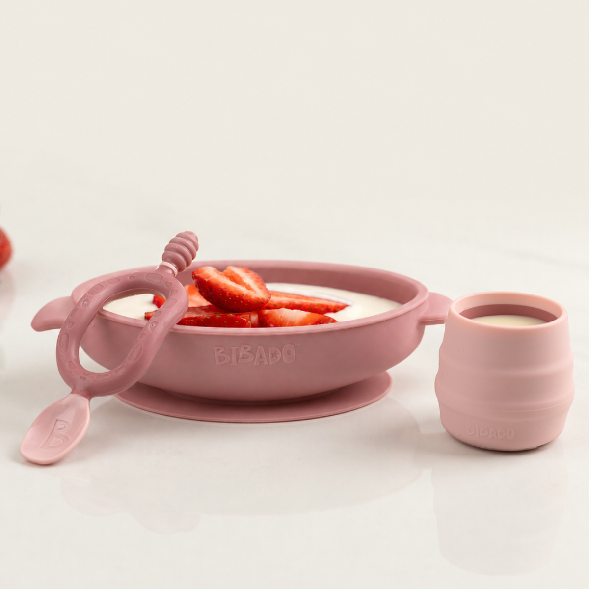 Pink silicone suction bowl with strawberries, matching training cup, and baby spoon. - Product image