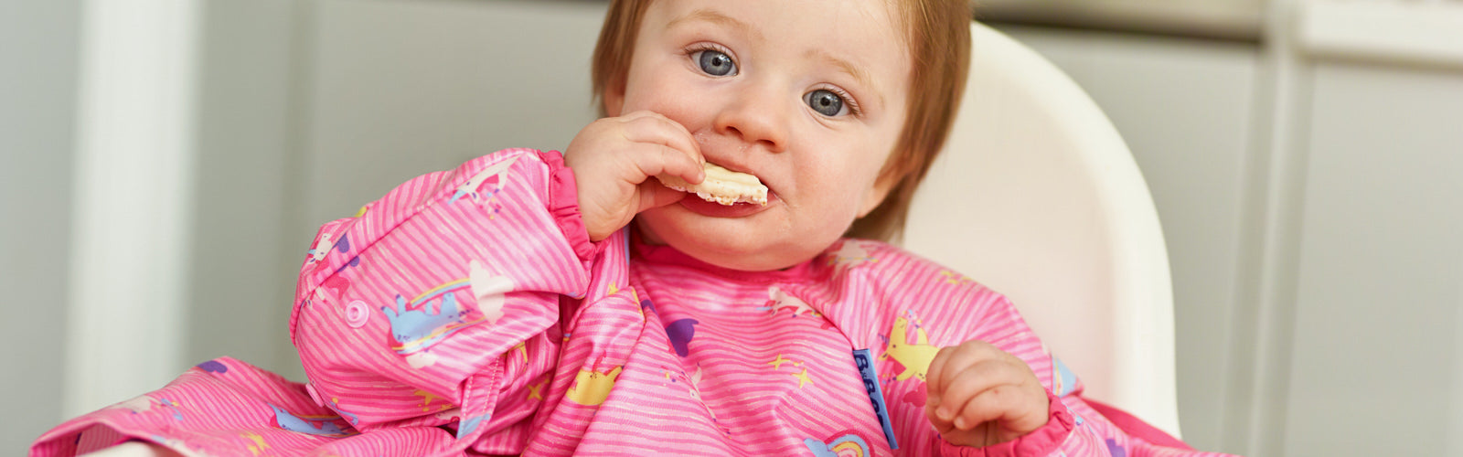 A baby in a pink bib happily eats a banana ghost snack.