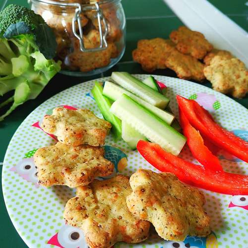 Flower-shaped broccoli & cheese biscuits on a plate with cucumber and red pepper sticks.
