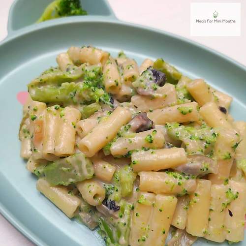 Creamy cheese and broccoli pasta with mushrooms on a light green plate.