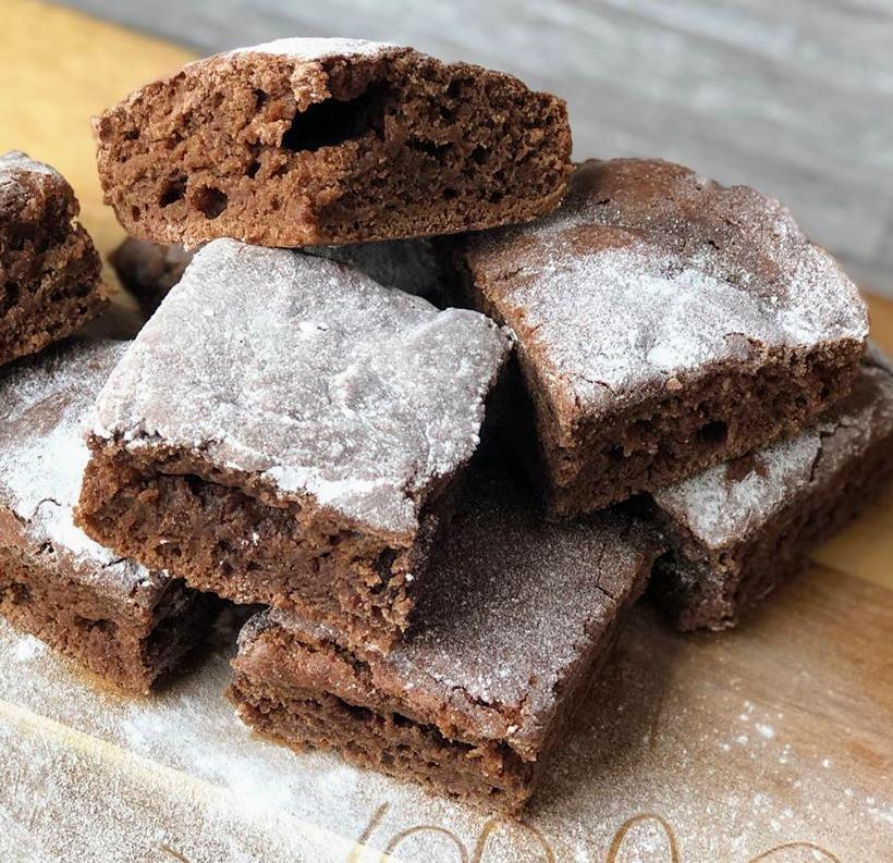 Stack of rich, fudgy vegan brownies dusted with icing sugar on a wooden board.