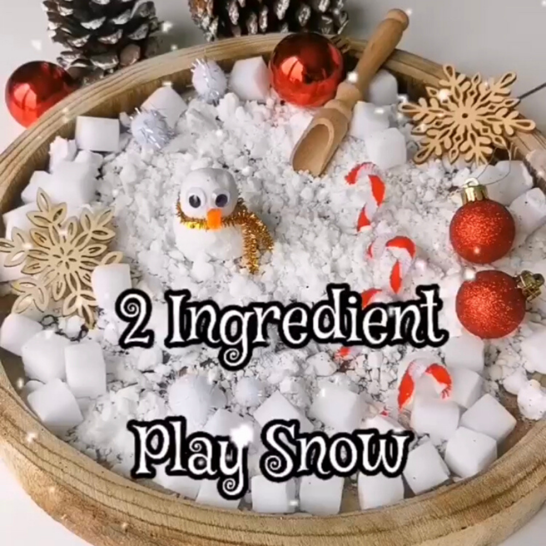 Wooden tray filled with white play snow, a snowman, candy canes, and Christmas decorations.