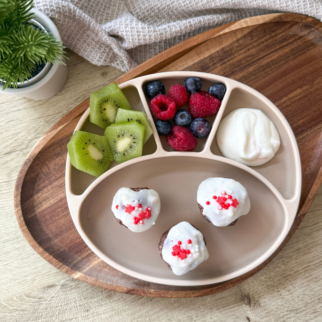 Three chocolate biscuit balls with white icing and red sprinkles, served with kiwi, berries, and yoghurt.