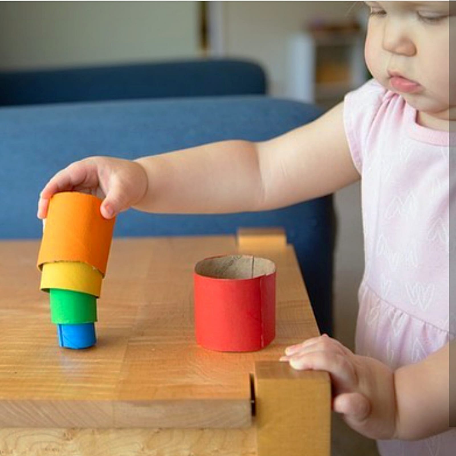 Toddler stacking DIY toilet roll cups in orange, yellow, green, and blue on a wooden table.