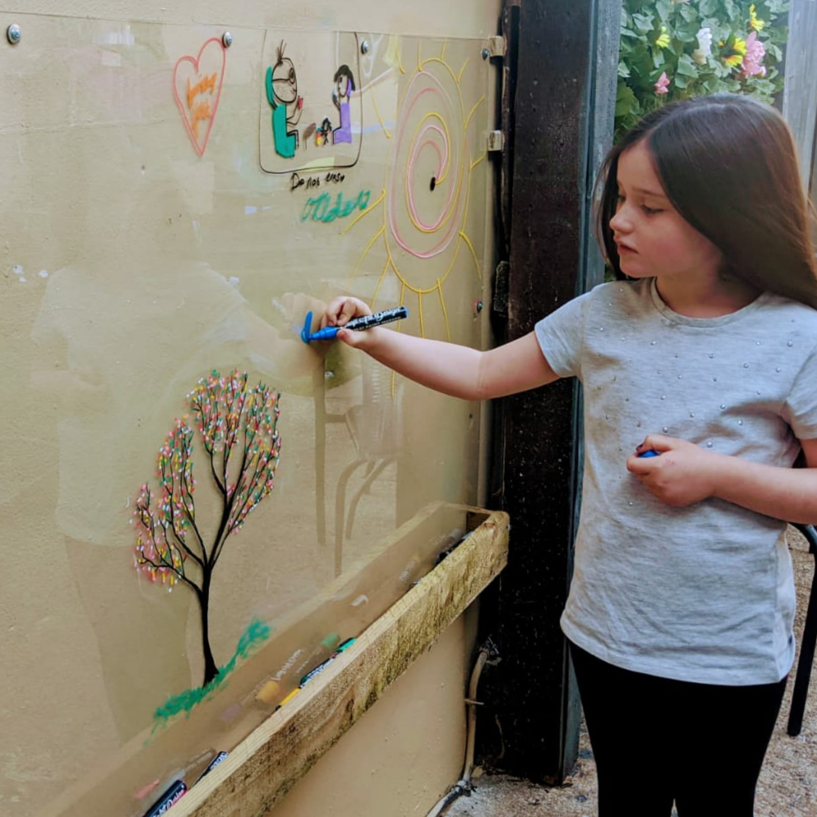 Young girl drawing colourful pictures on a DIY outdoor perspex drawing board.