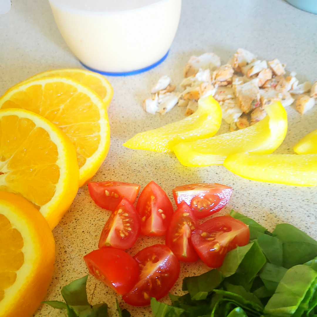 Chopped oranges, tomatoes, spinach, yellow peppers, and chicken, with a jug of milk.
