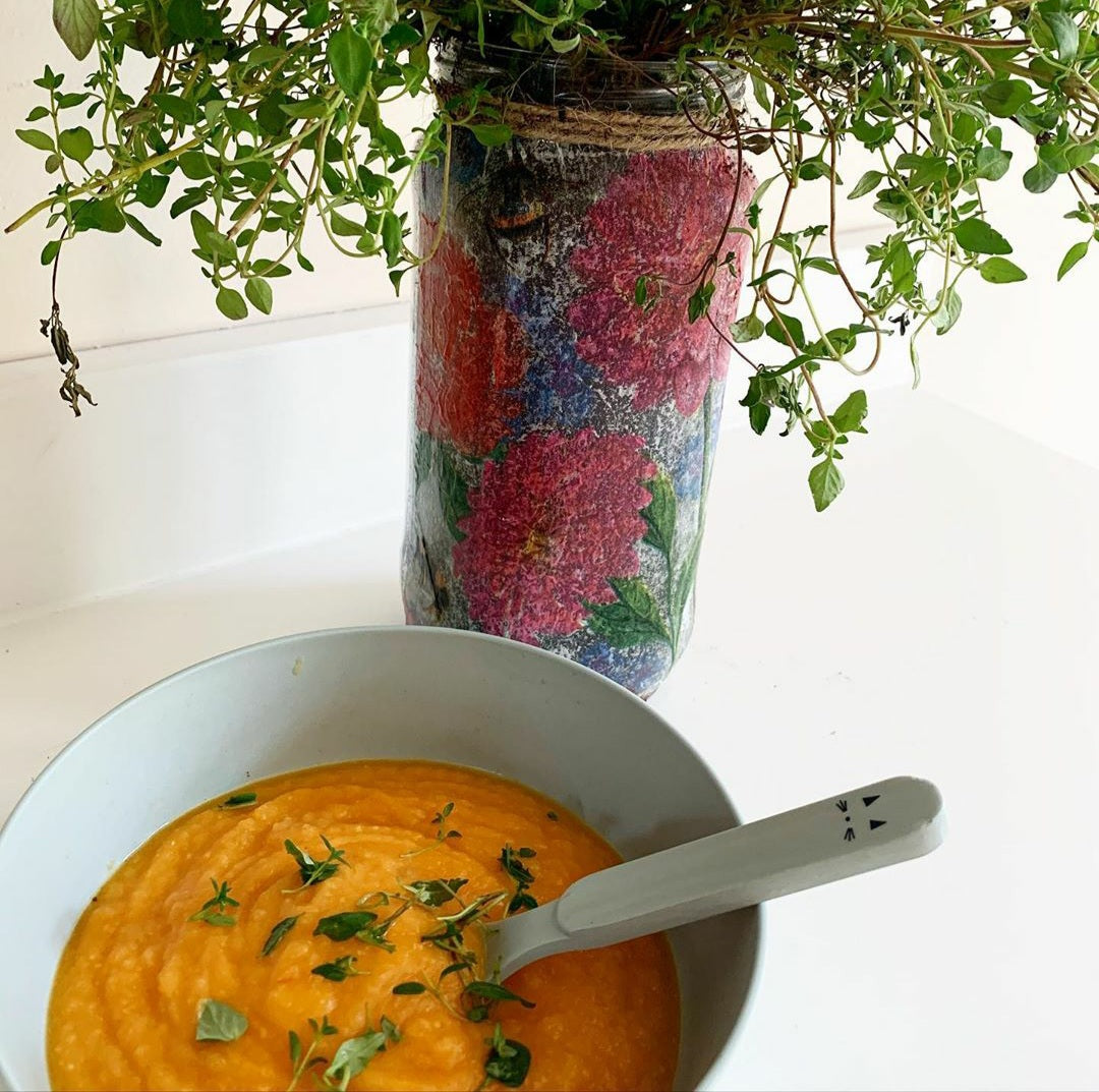 A light blue bowl of orange lentil soup garnished with fresh thyme, next to a floral vase.