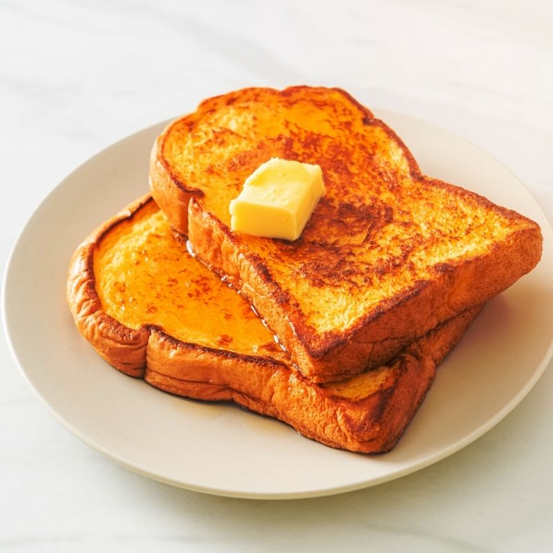 Two golden maple French toast slices with a pat of butter on a white plate.