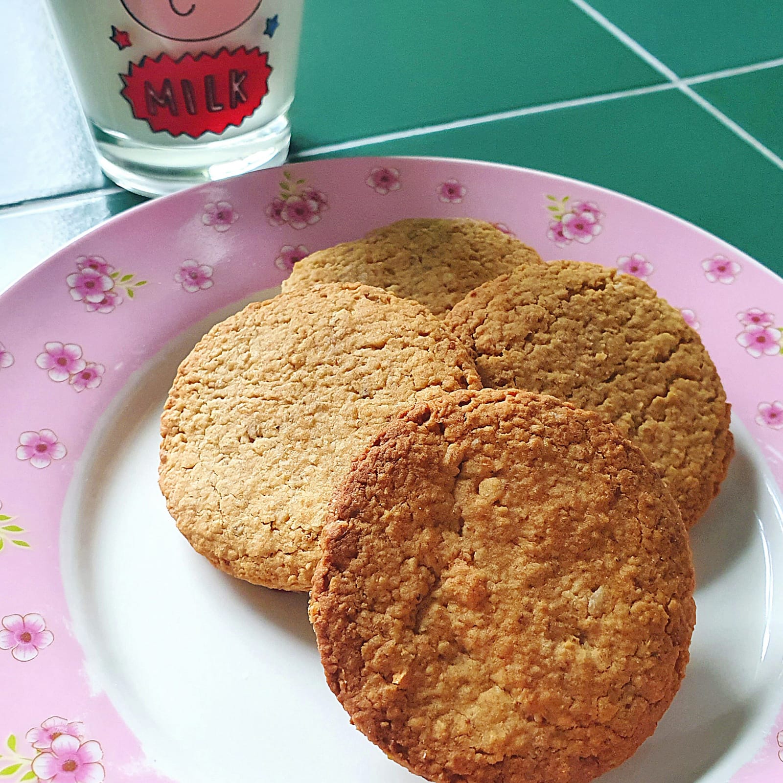 Golden-brown honey oat biscuits on a pink floral plate with a glass of milk.