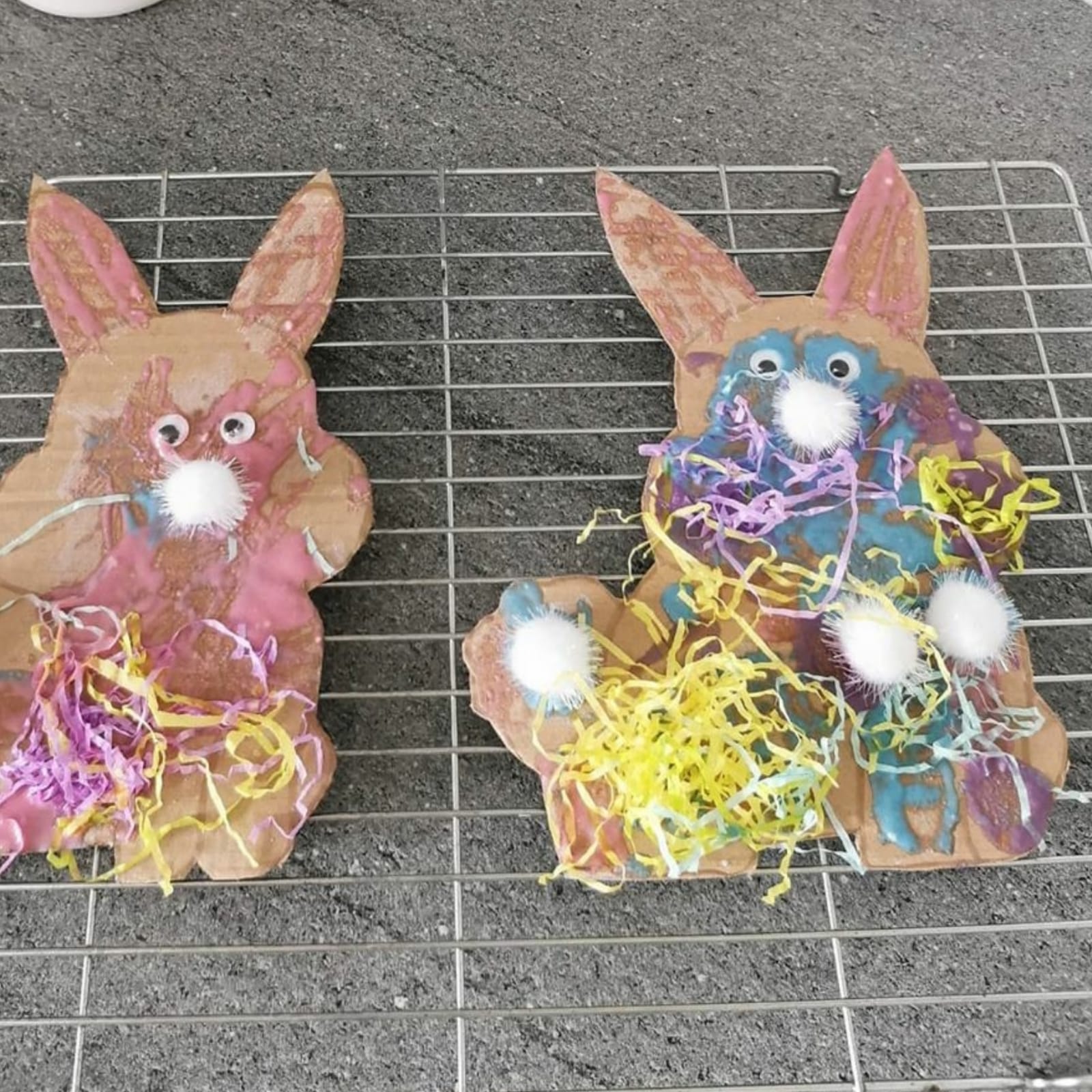 Two cardboard bunnies decorated with colourful edible paint, pom-poms, and shredded paper.