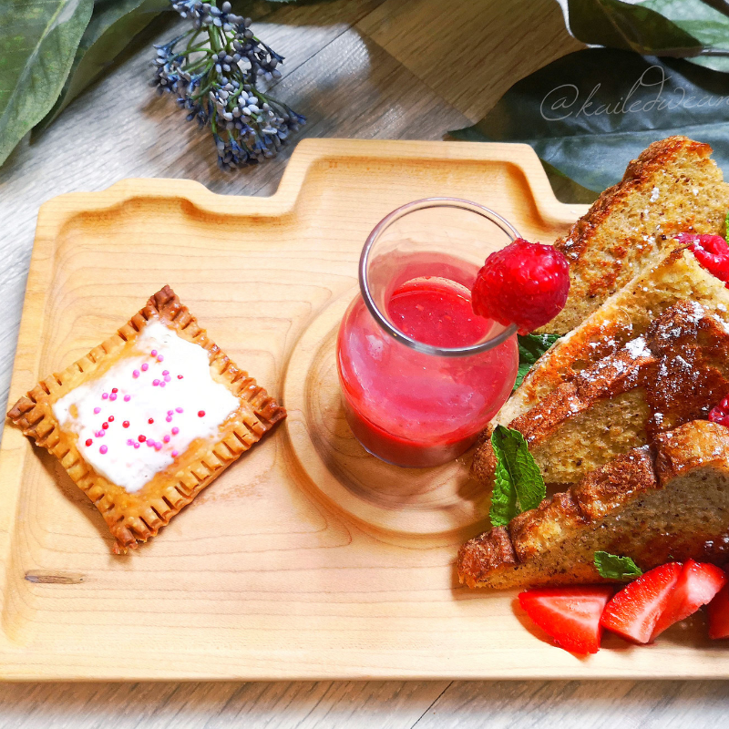 Golden homemade poptart with sprinkles, French toast, berries, and a pink drink on a wooden tray.