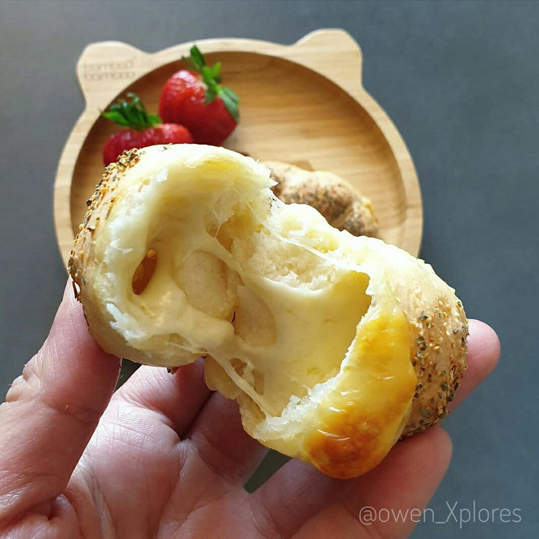 Hand holding a cheesy bread roll, torn open to reveal gooey melted cheese.