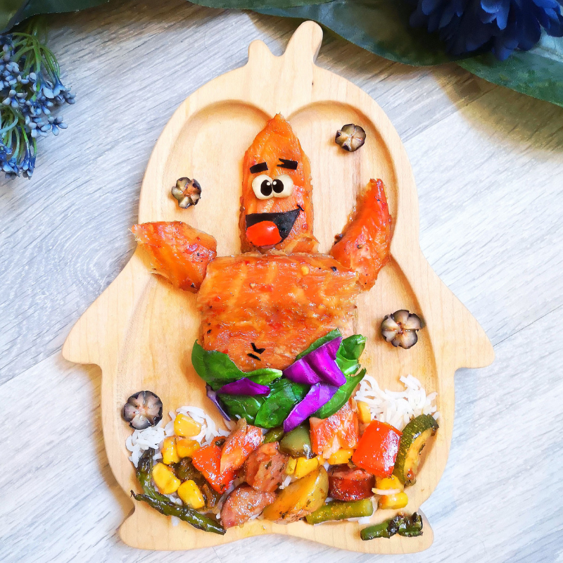 Fun rainbow tray bake shaped like Patrick Star on a wooden plate, with colourful vegetables and rice.