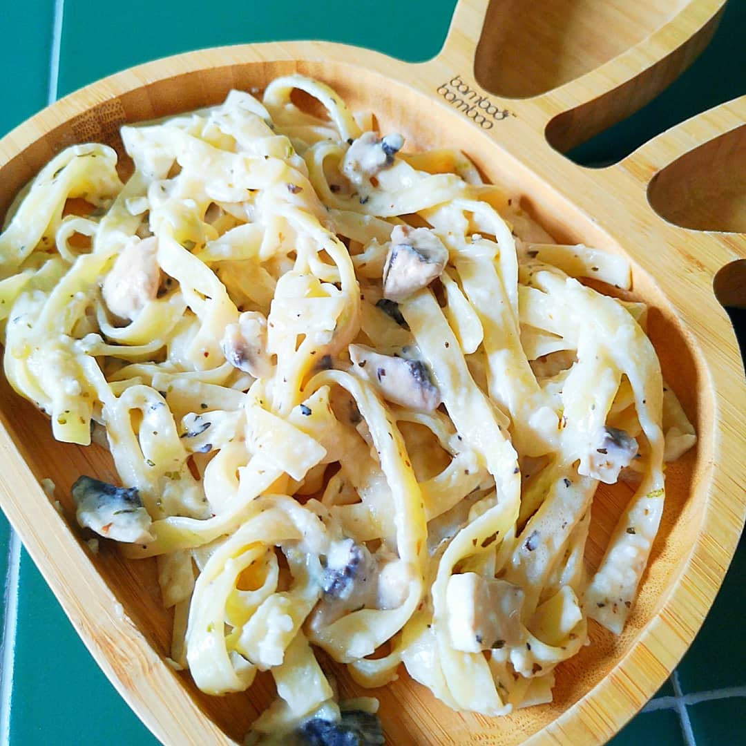 Creamy mushroom linguine in a wooden bowl on a green tiled surface.