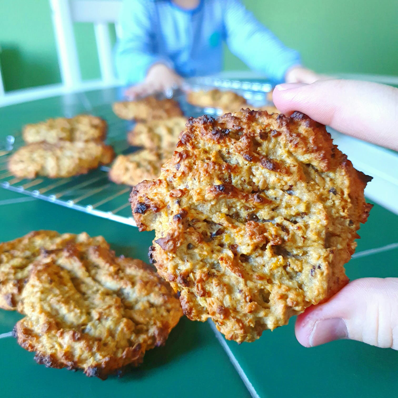 Hand holding a freshly baked, golden-brown "Super Power Cookie" with more on a cooling rack.