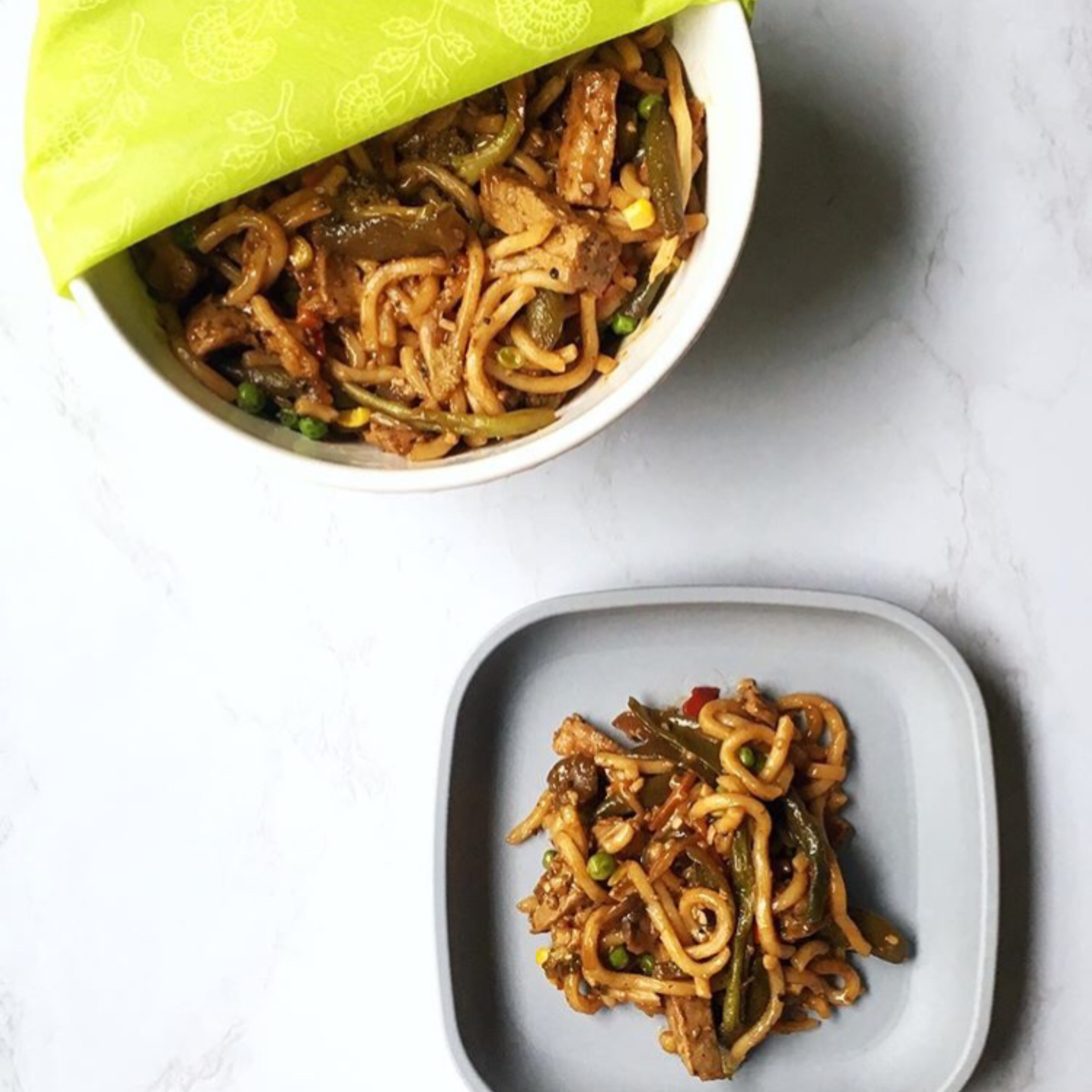 Stir-fry noodles with vegetables and meat in a white bowl and on a grey plate.