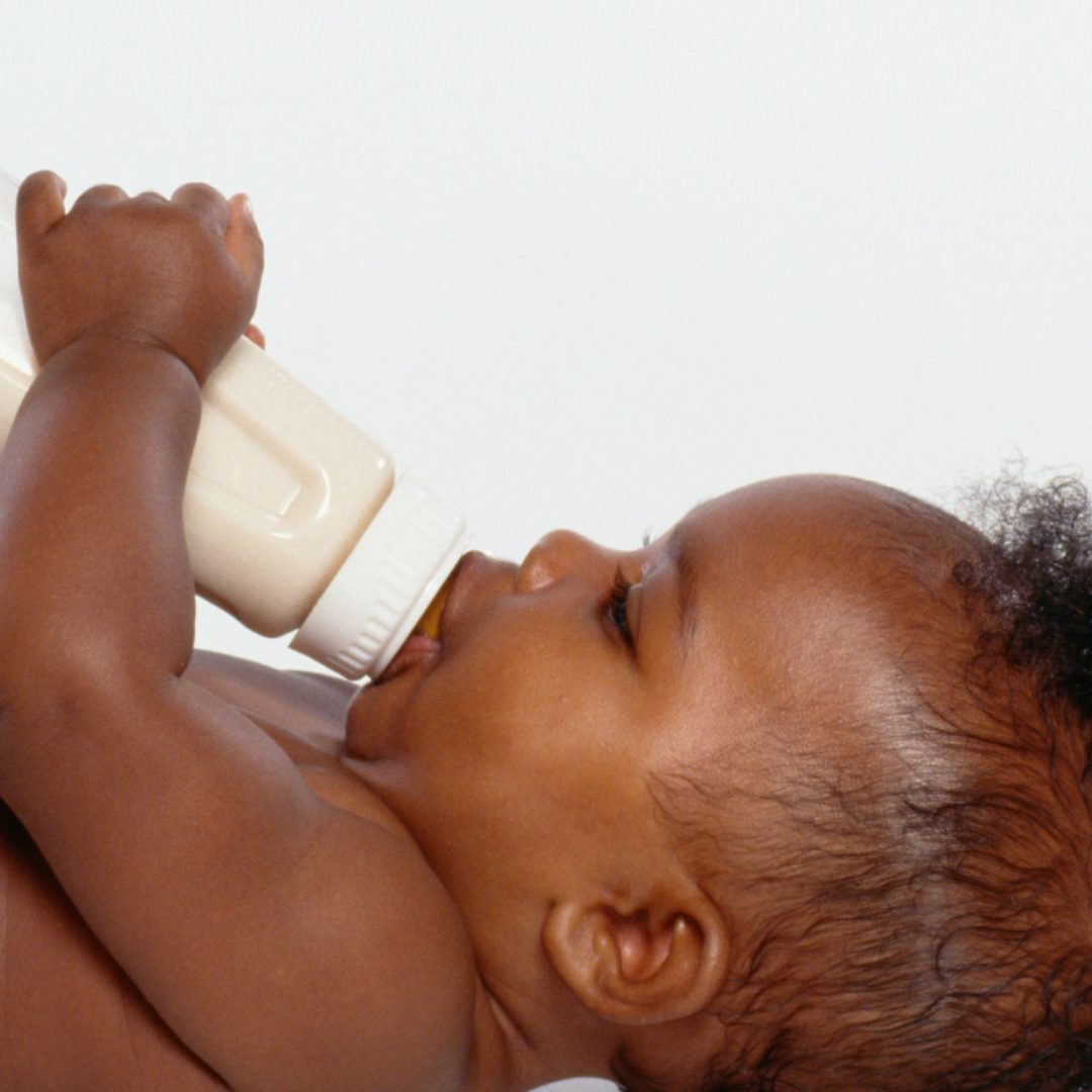 Close-up of a baby lying down, drinking milk from a white bottle.