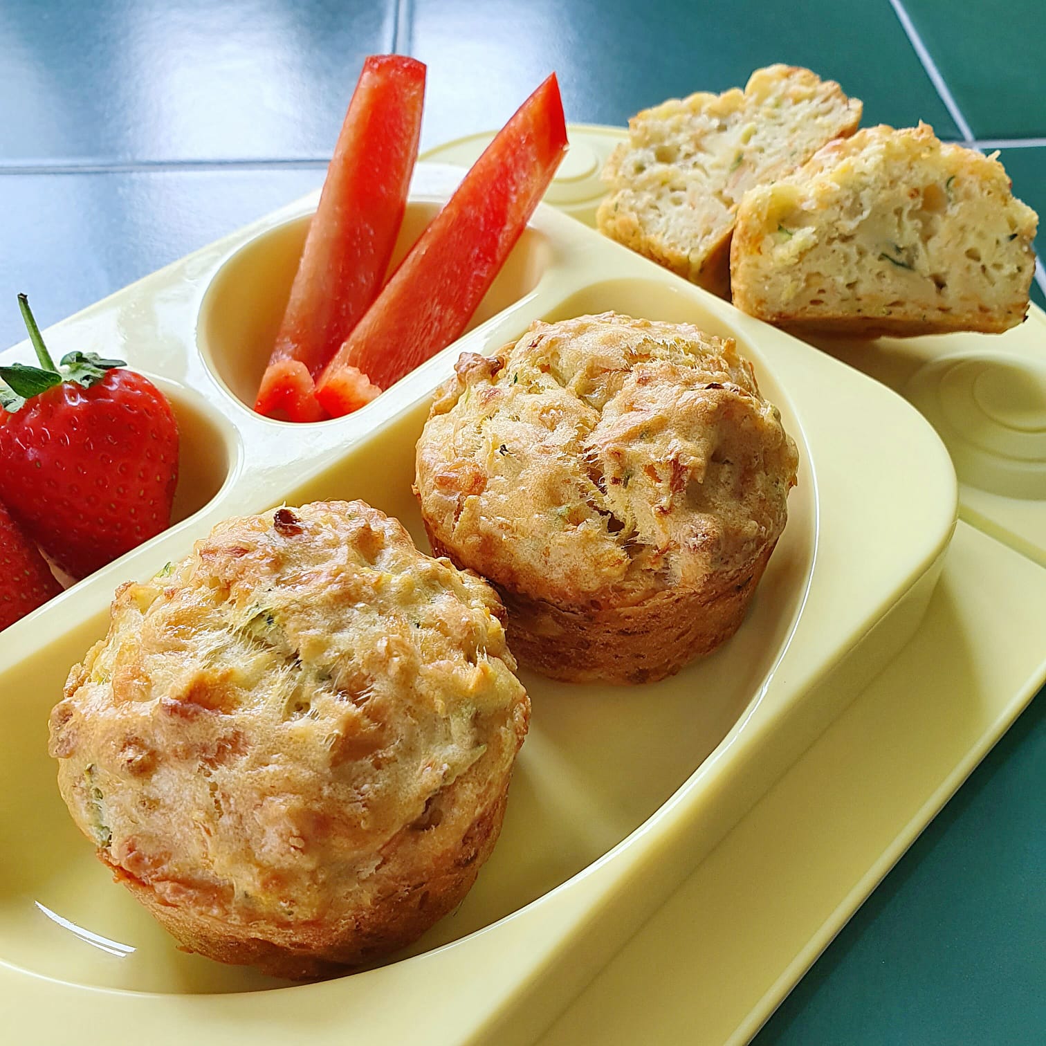 Two savoury muffins with strawberries and red pepper sticks on a yellow children's plate.