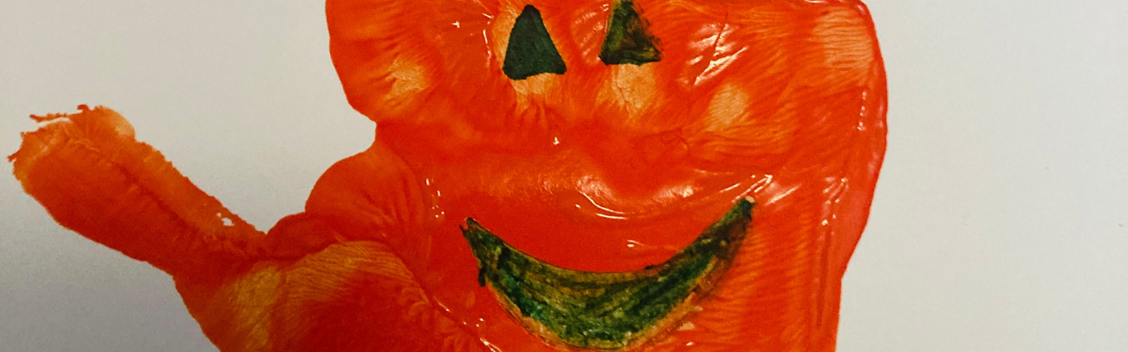 A child's orange handprint pumpkin with green painted eyes and a smiling mouth.