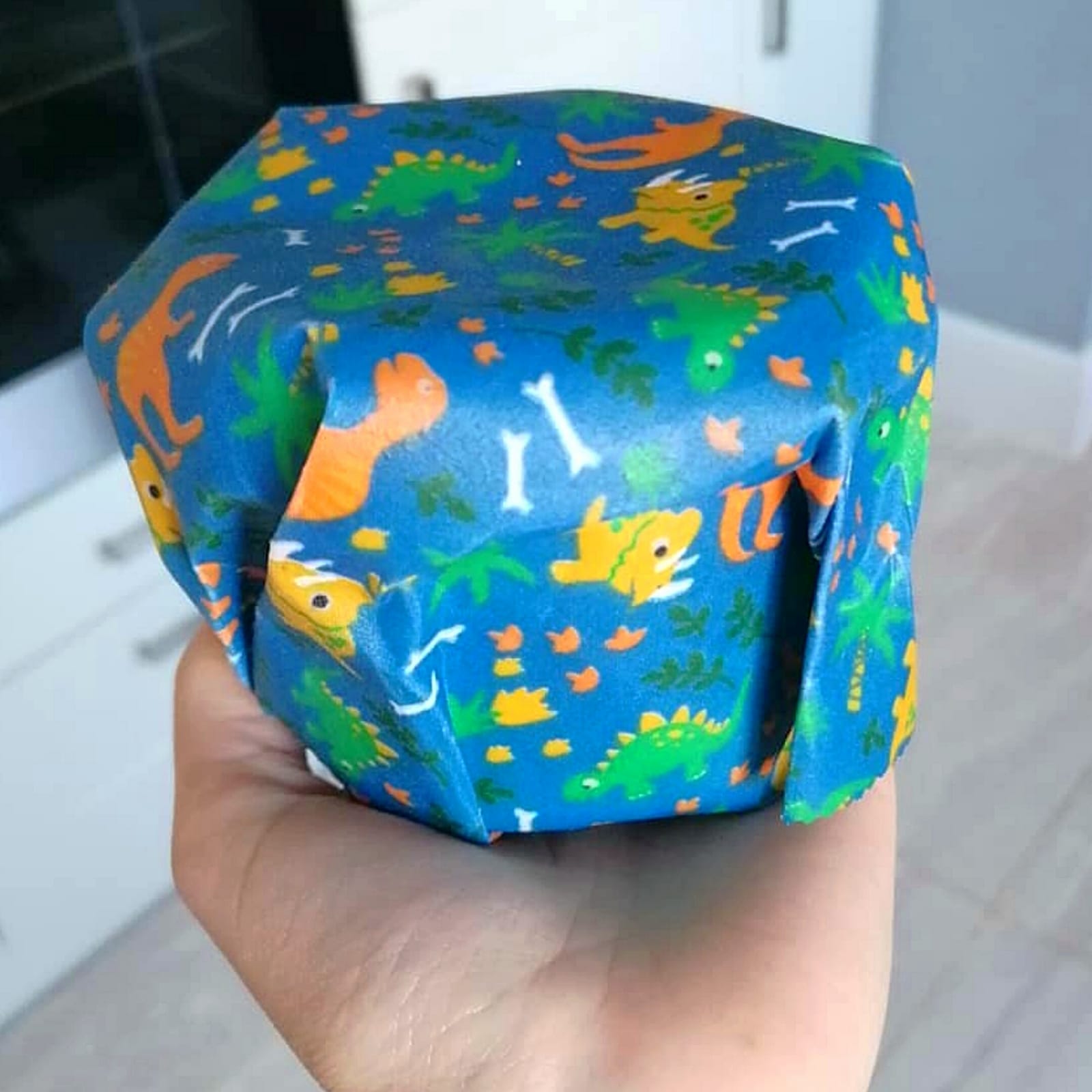 Hand holding a blue beeswax wrap with colourful dinosaur and bone patterns.
