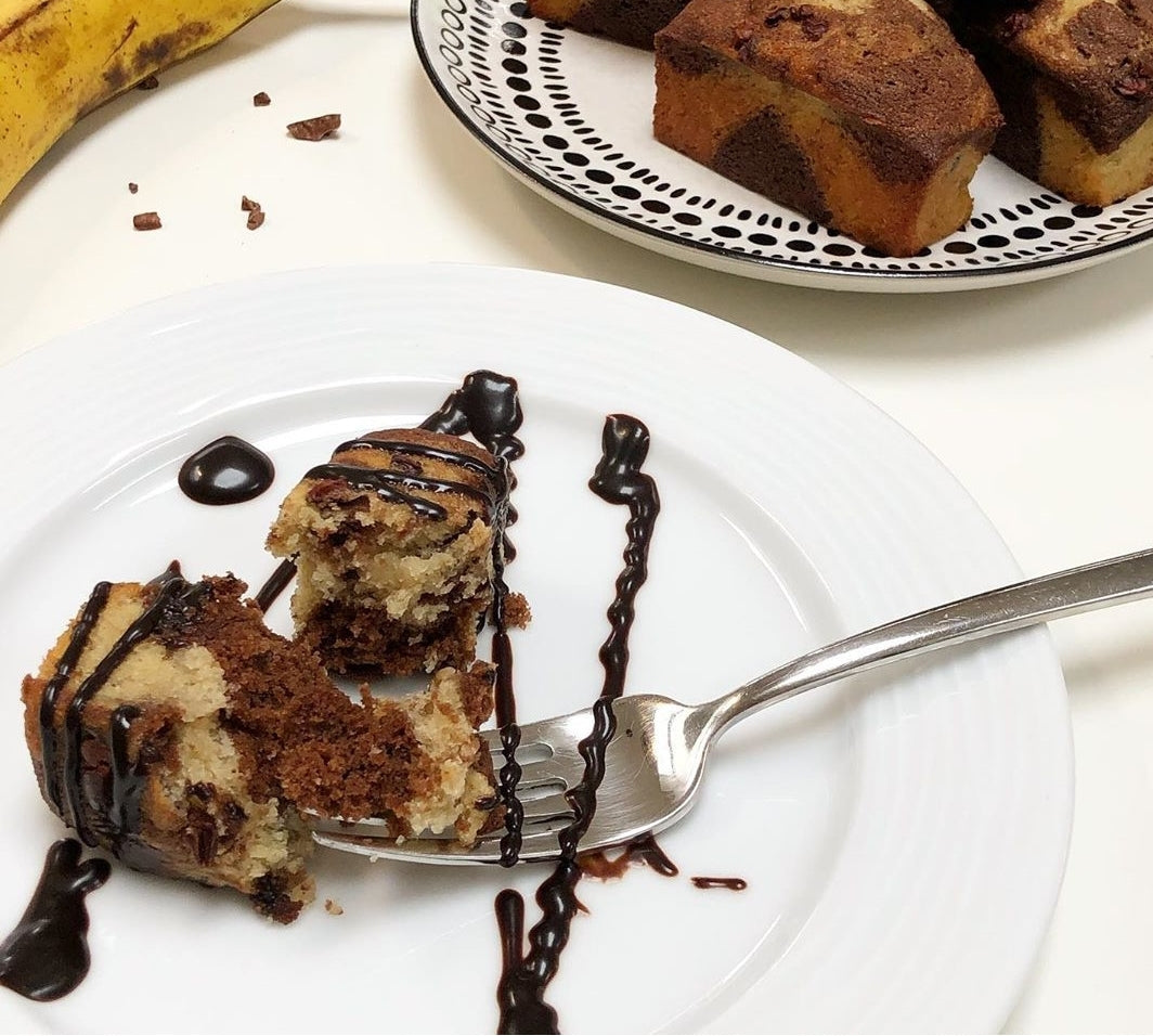 Marbled banana and chocolate mini loaves, one drizzled with sauce and partially eaten on a white plate.