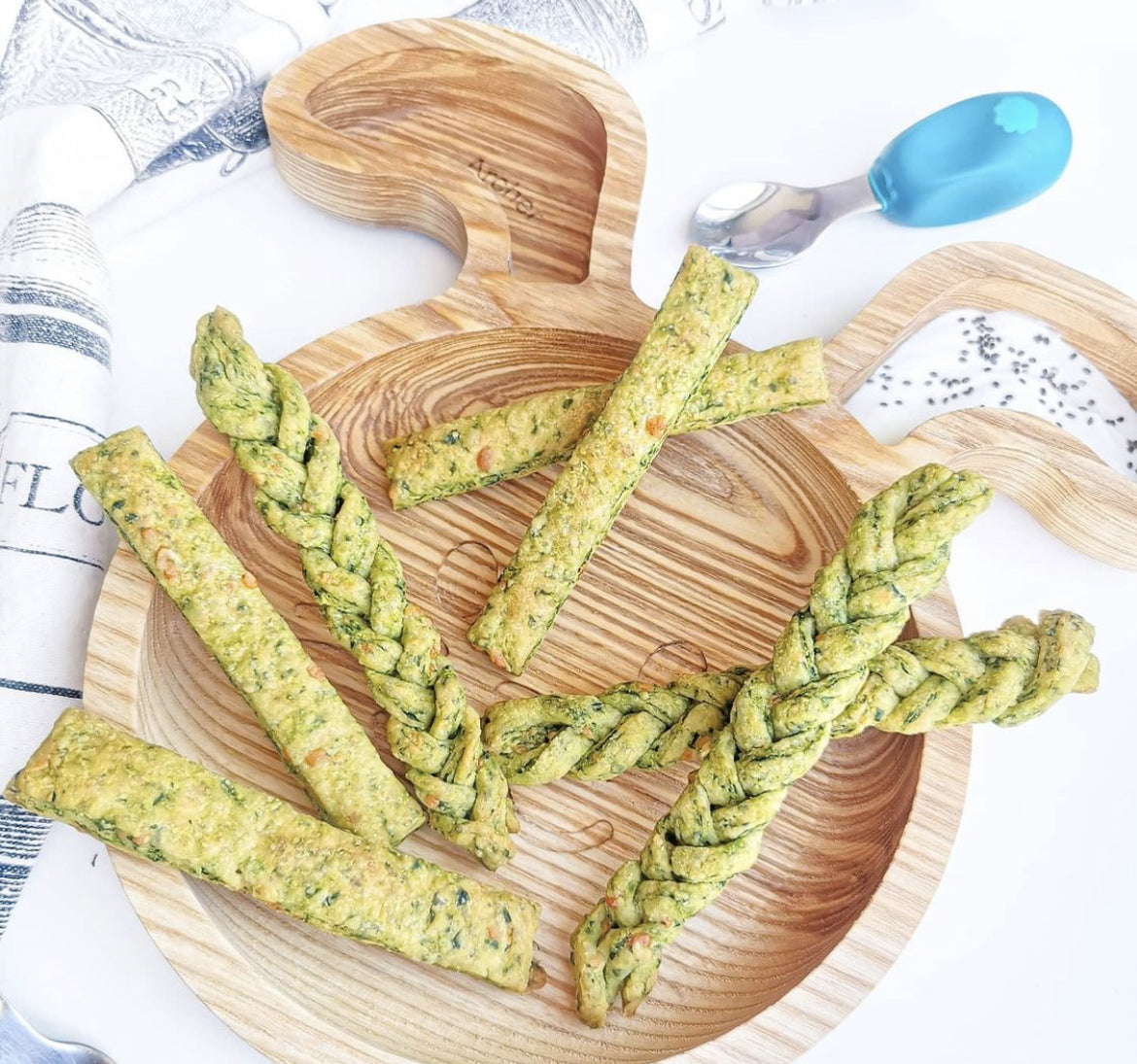 Green spinach and cheddar straws, some braided, on a wooden bunny-shaped plate.
