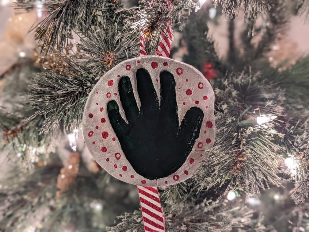 White salt dough decoration with a black handprint and red polka dots, hanging on a Christmas tree.