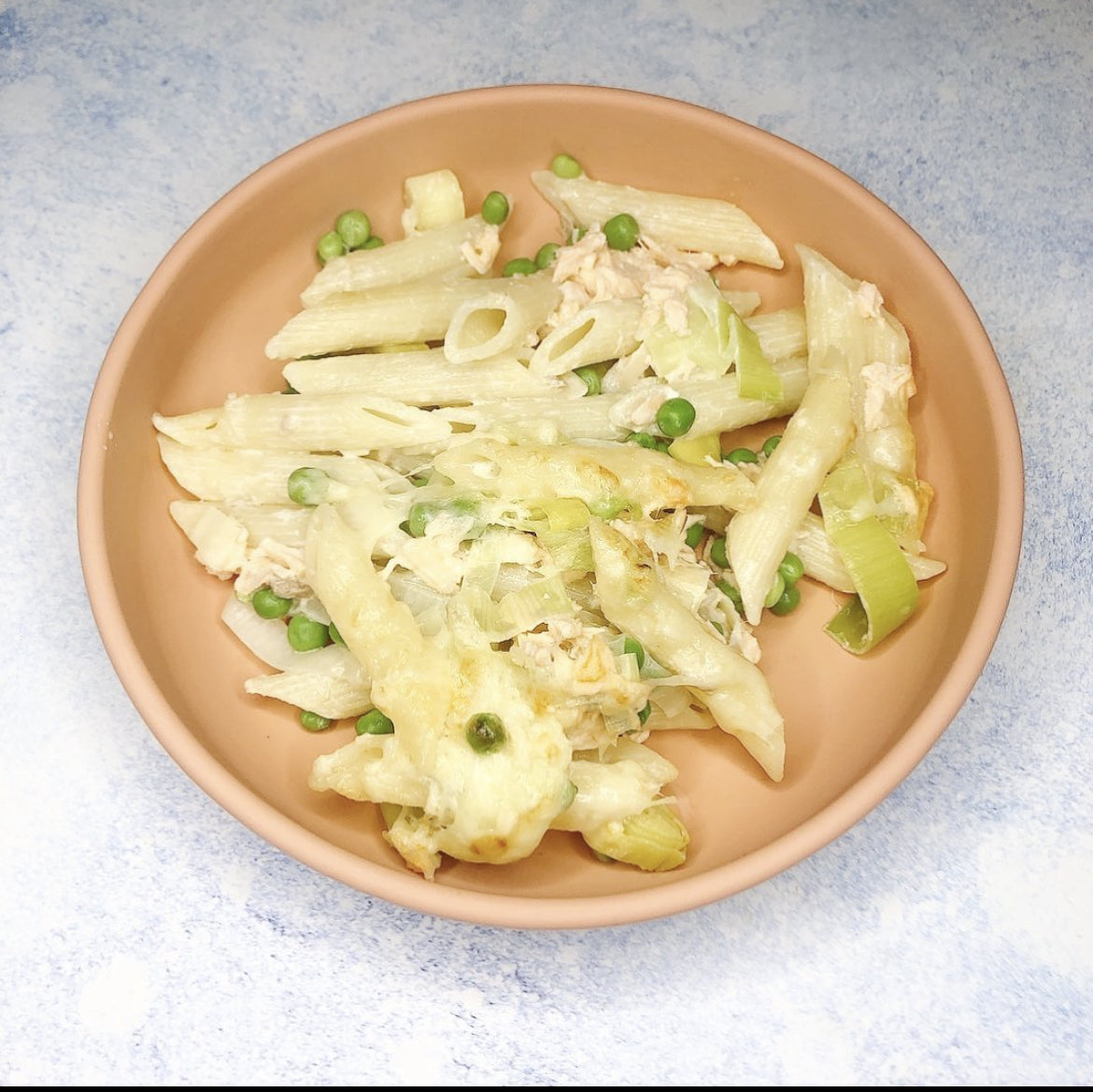 Creamy salmon and leek penne pasta with green peas in a terracotta bowl.