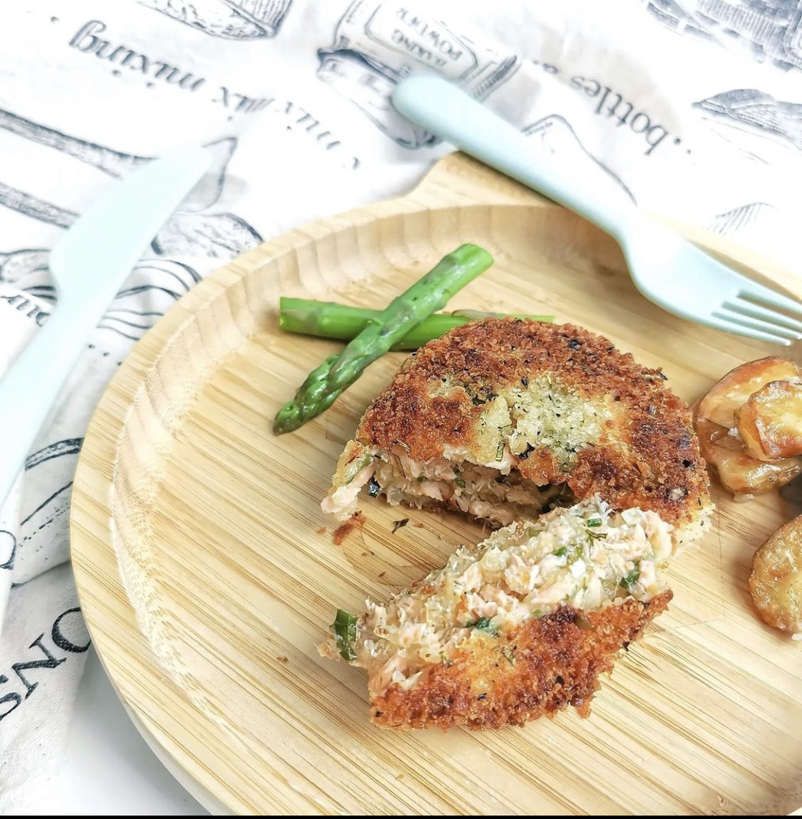 Golden-brown salmon fishcake, cut open to show flaky pink fish, served with asparagus on a wooden plate.